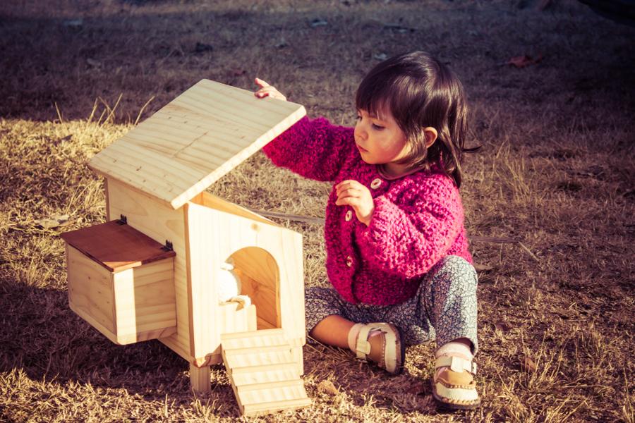 Niña jugando con un gallinero de juguete de madera