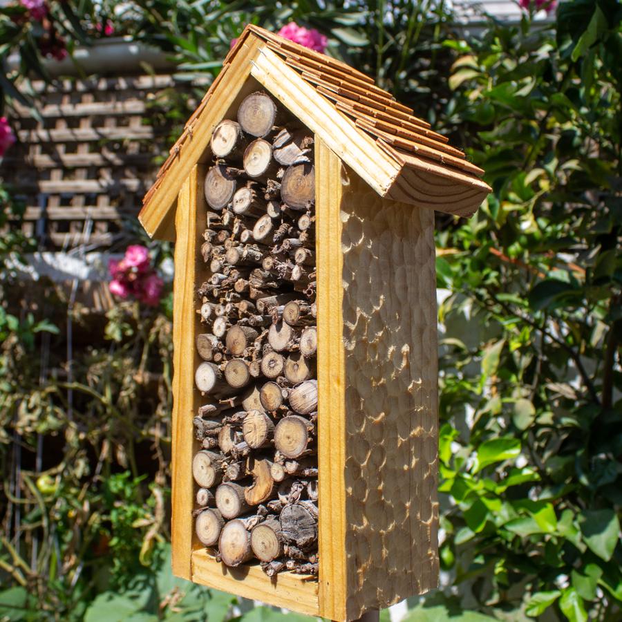 Hotel de insectos relleno de ramas cortadas con techo de tejuelas